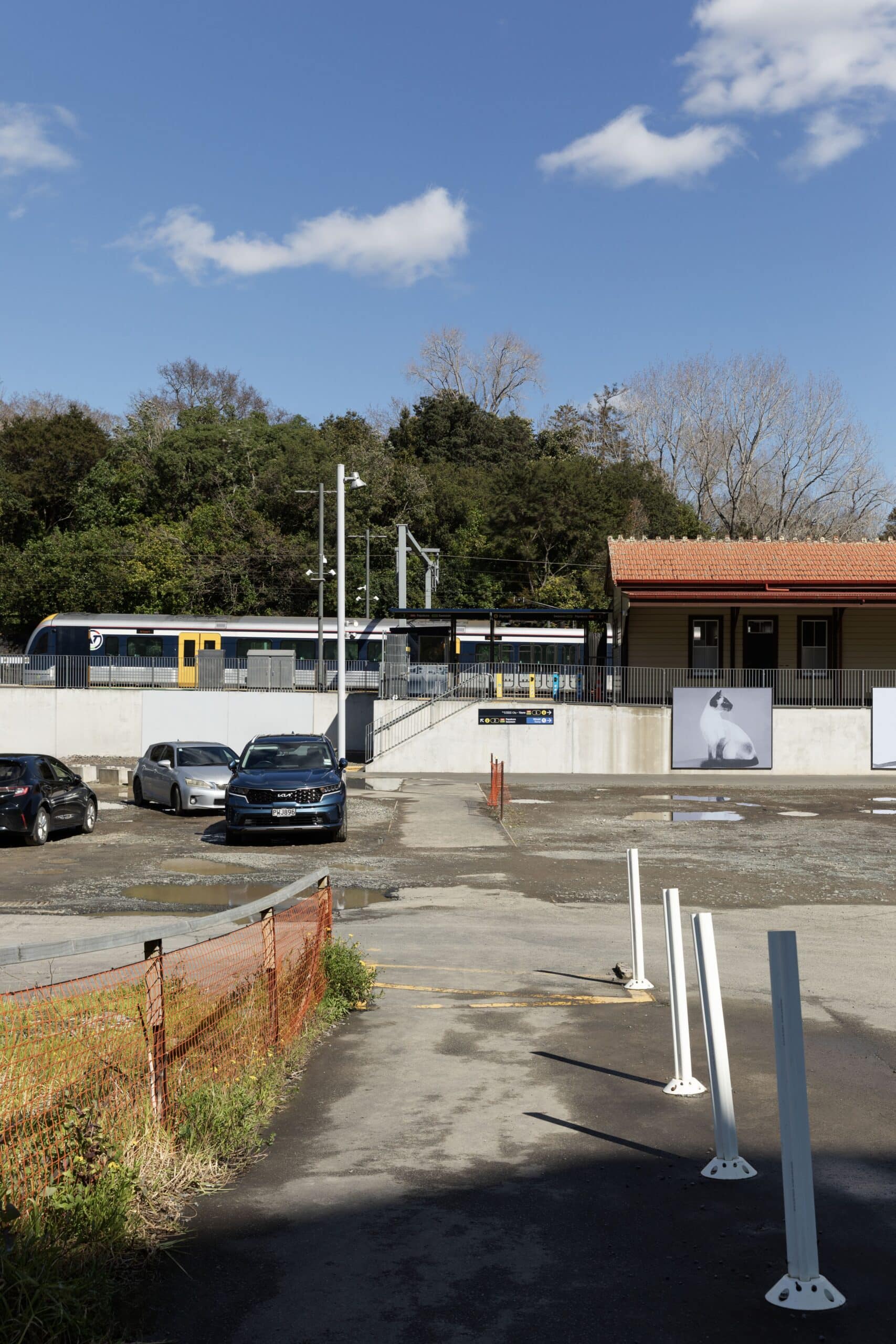 A pathway marked by bollards crosses a car park leading toward a train station platform.